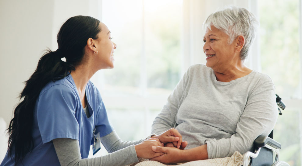 nursing_care_rehab_image (1) A nurse sits with a senior woman and smiles.